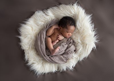 Newborn boy in brown wrap on a big pillow of cream fur