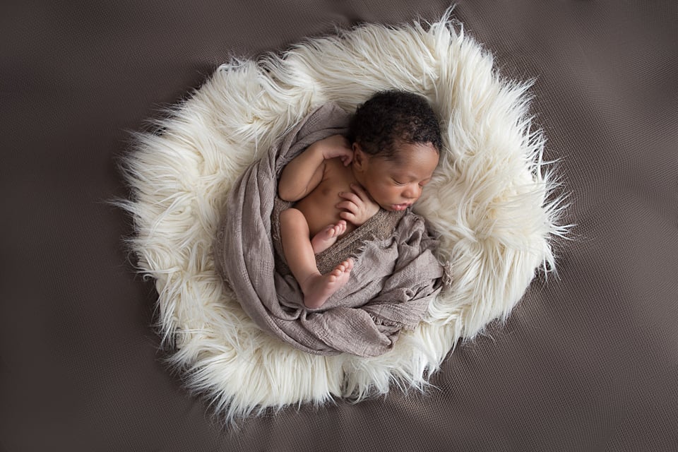 Newborn boy in brown wrap on a big pillow of cream fur