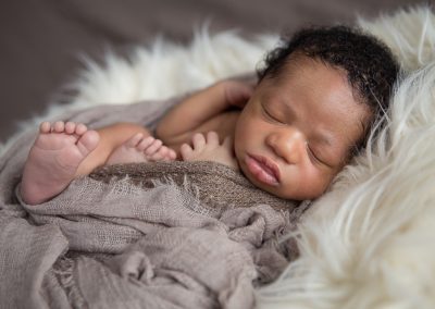 African american newborn boy in brown blanket on cream fur layer in Suwanee photo studio of Colleen Hight