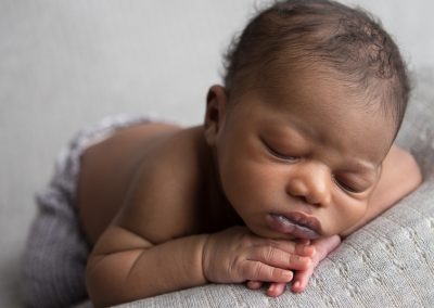 Newborn baby in gray pants with chin resting on hands in Suwanee, Ga studio