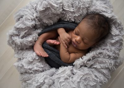 Newborn Boy lying on back in basket with gray textured blankets in Suwanee studio