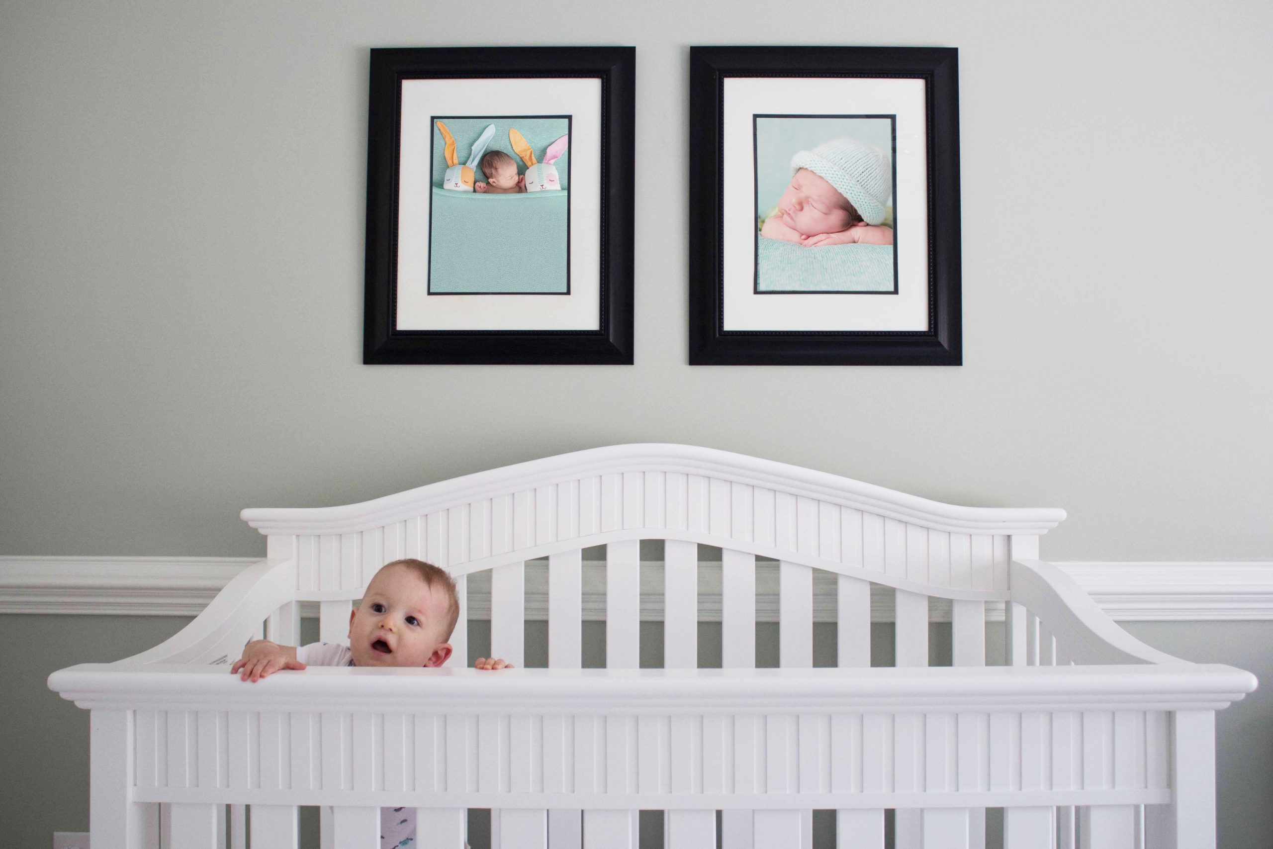 Lifestyle picture of a baby in a crib in front of studio newborn pictures on the wall
